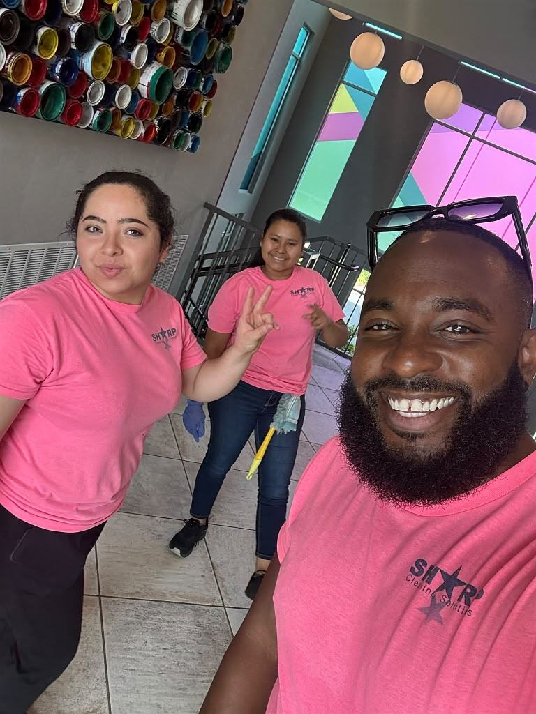 Three Sharp Cleaning team members in branded pink shirts on site, one holding a duster