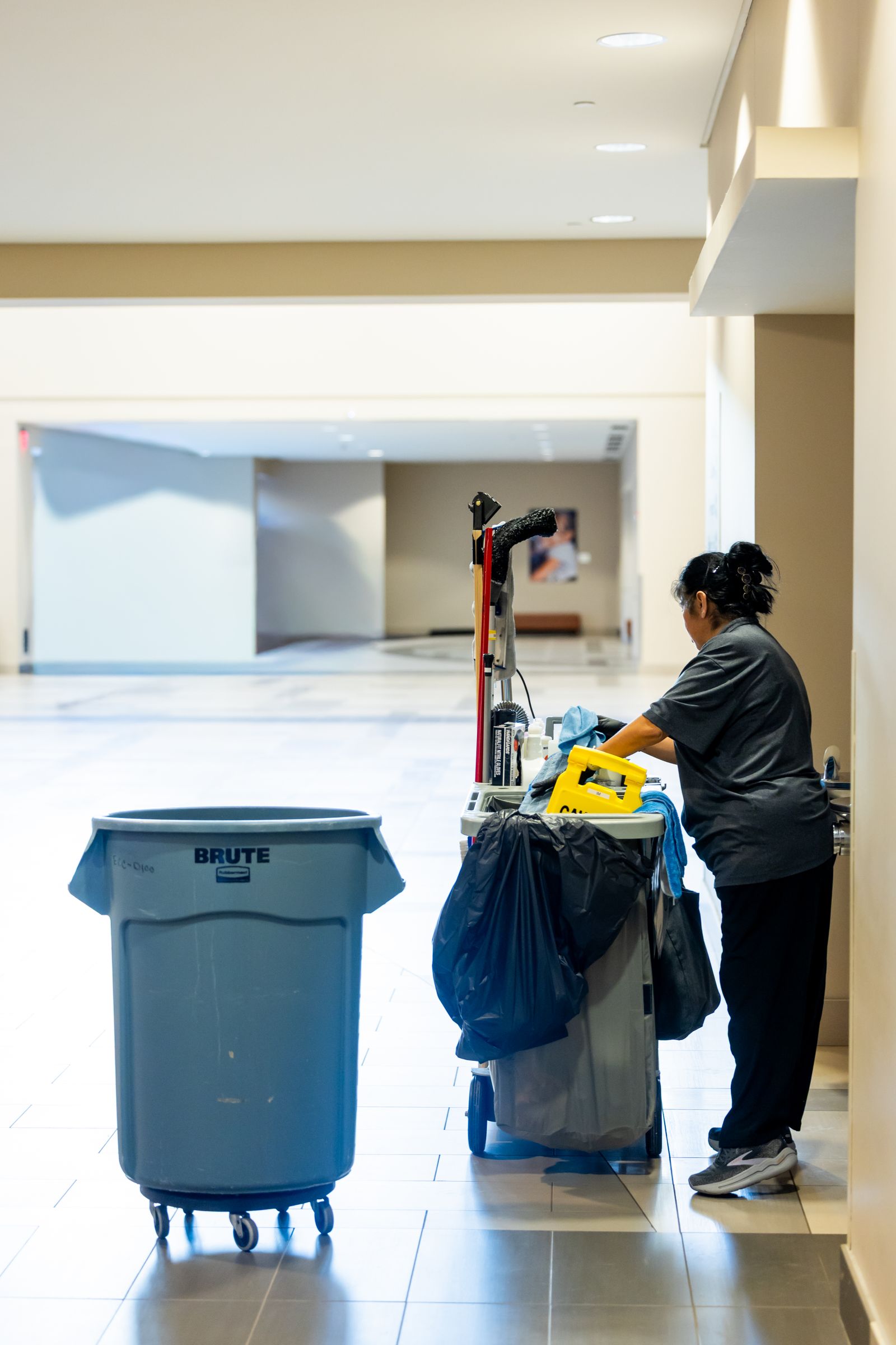 Janitorial worker pushing a cleaning cart in a commercial hallway